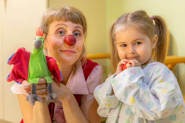 Ein kleines Mädchen mit einer roten Nase in der Hand neben Clownin Lilo und ihrer Handpuppe.