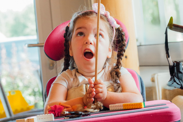 Ein Mädchen im Rollstuhl balanciert einen Teller auf einem Stäbchen.