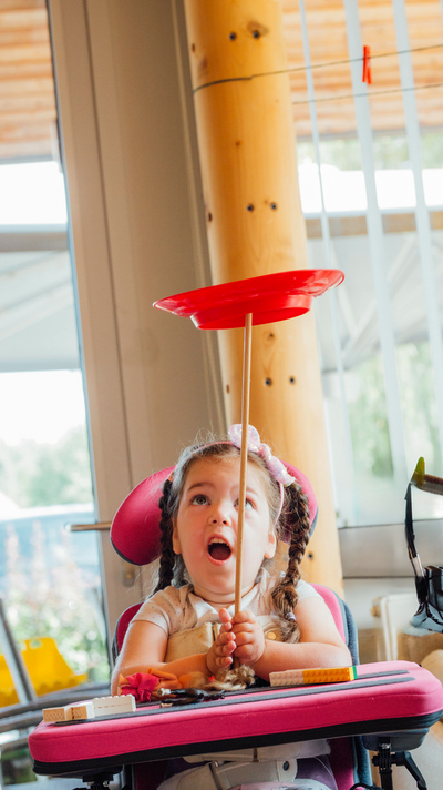 Ein Mädchen im Rollstuhl balanciert einen Teller auf einem Stäbchen.