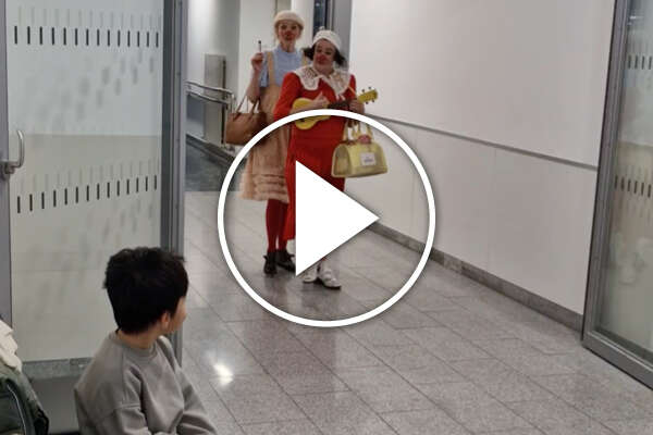 Eine Junge auf dem Krankenhausflur beobachtet zwei musizierende Clowninnen.