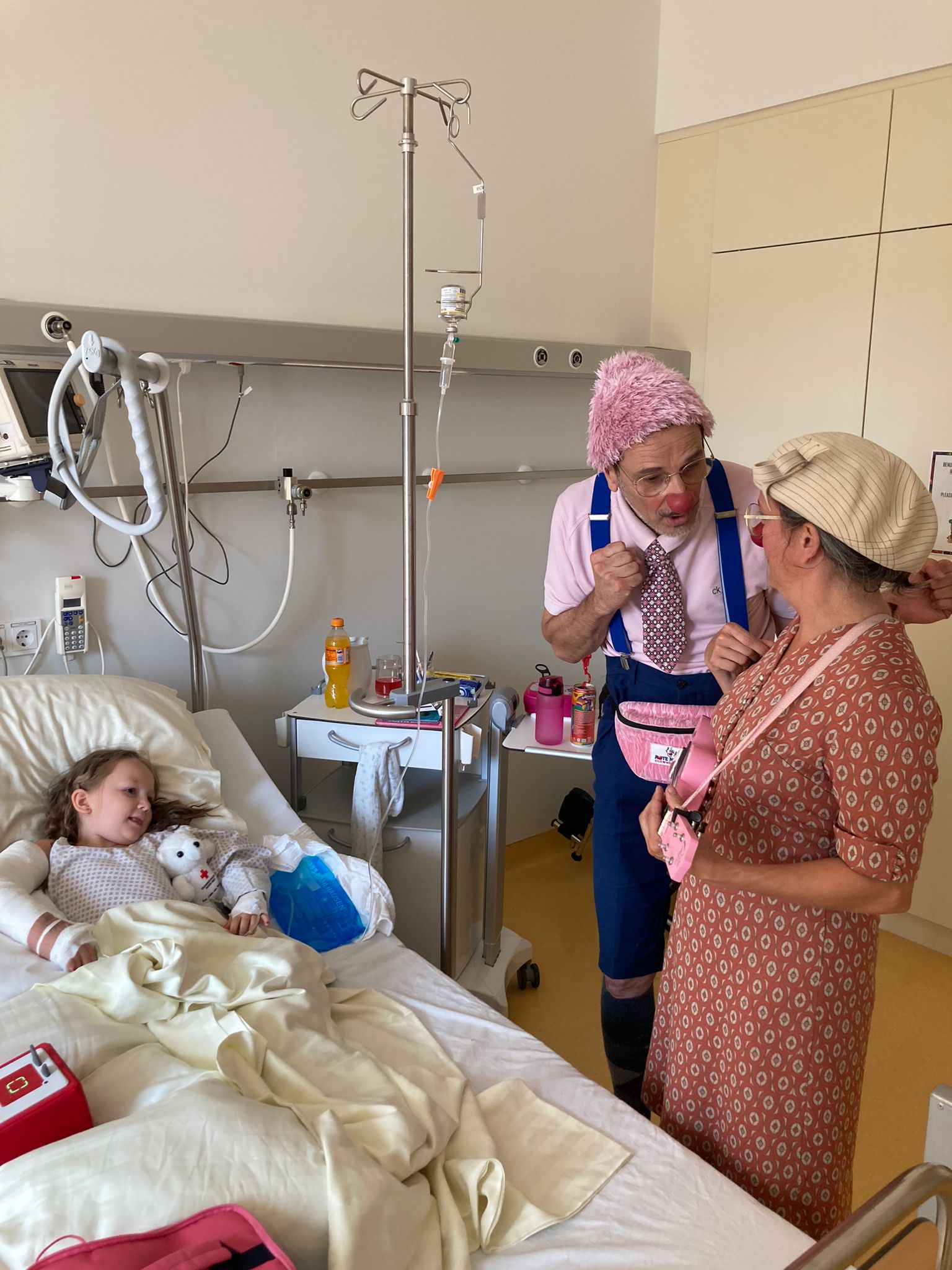Das Mädchen Frida liegt im Krankenbett und schaut zwei Clowns zu.